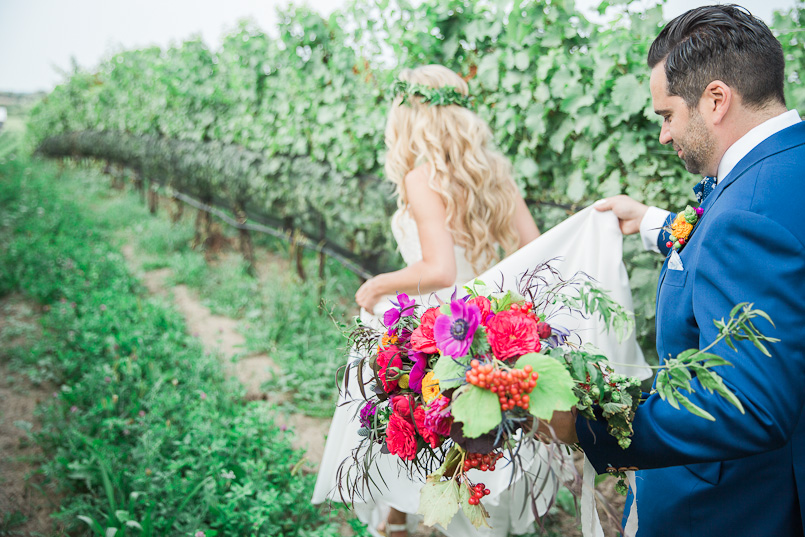 groom helps his bride with her dress and colourful bouquet