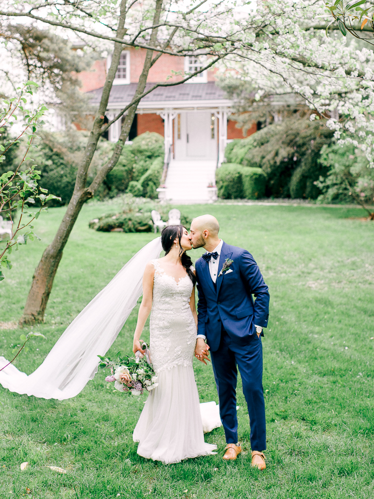 bride and groom kiss in front of kurtz orchard house with cherry blossoms