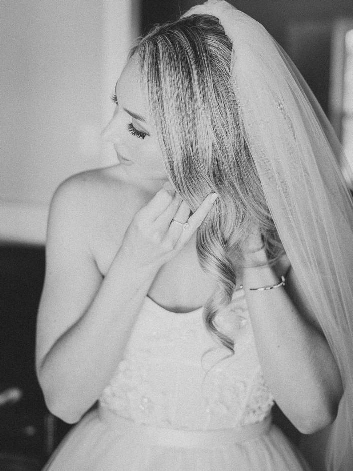 black and white photo of a bride putting on her earings